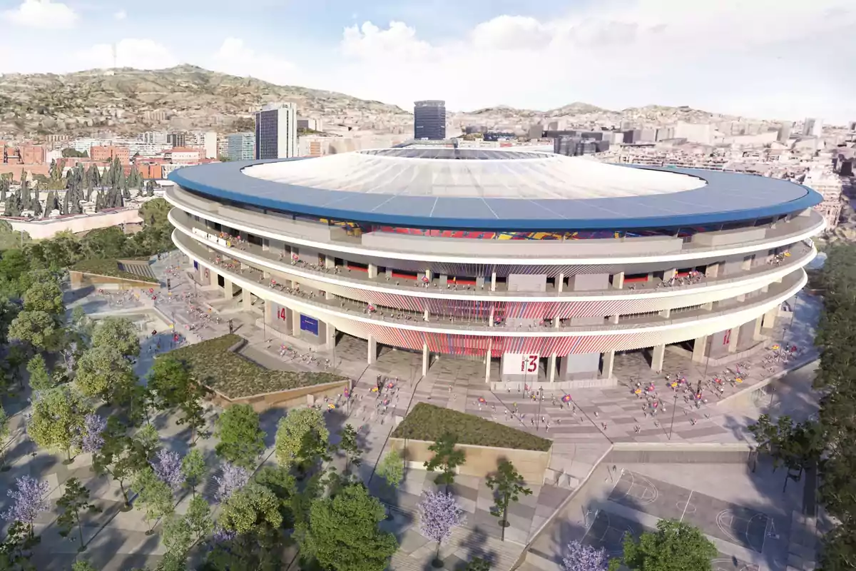Vista aérea de un estadio moderno rodeado de árboles y edificios en una ciudad con colinas al fondo.