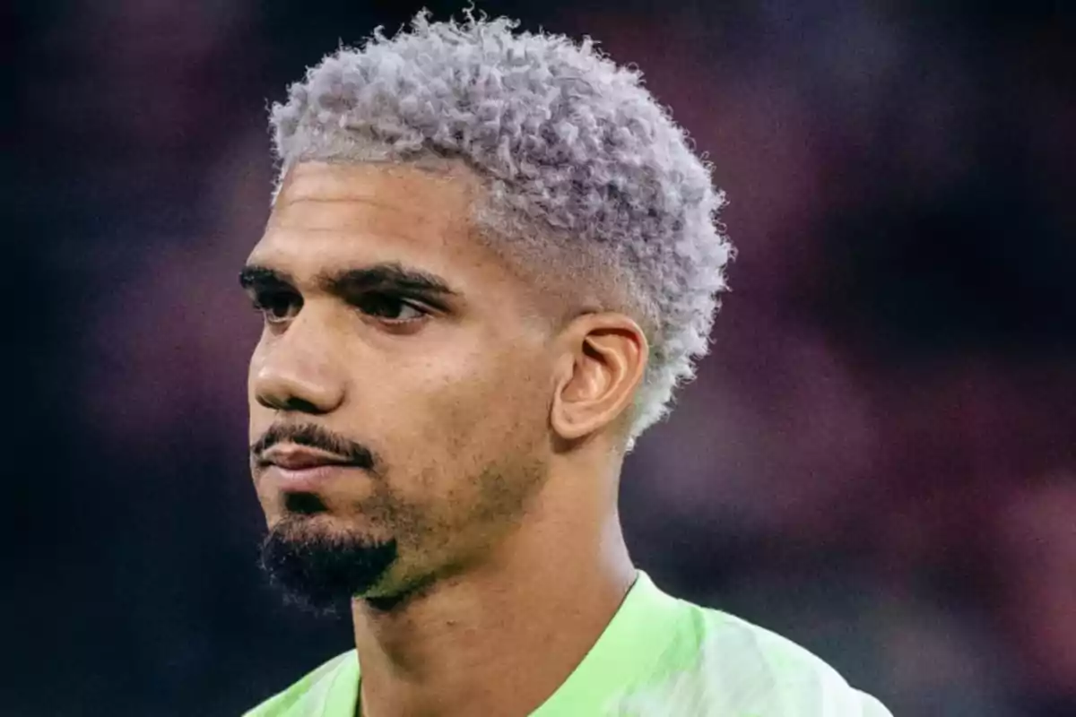 Curly-haired man with dyed gray hair, short beard, and green t-jersey looking straight ahead
