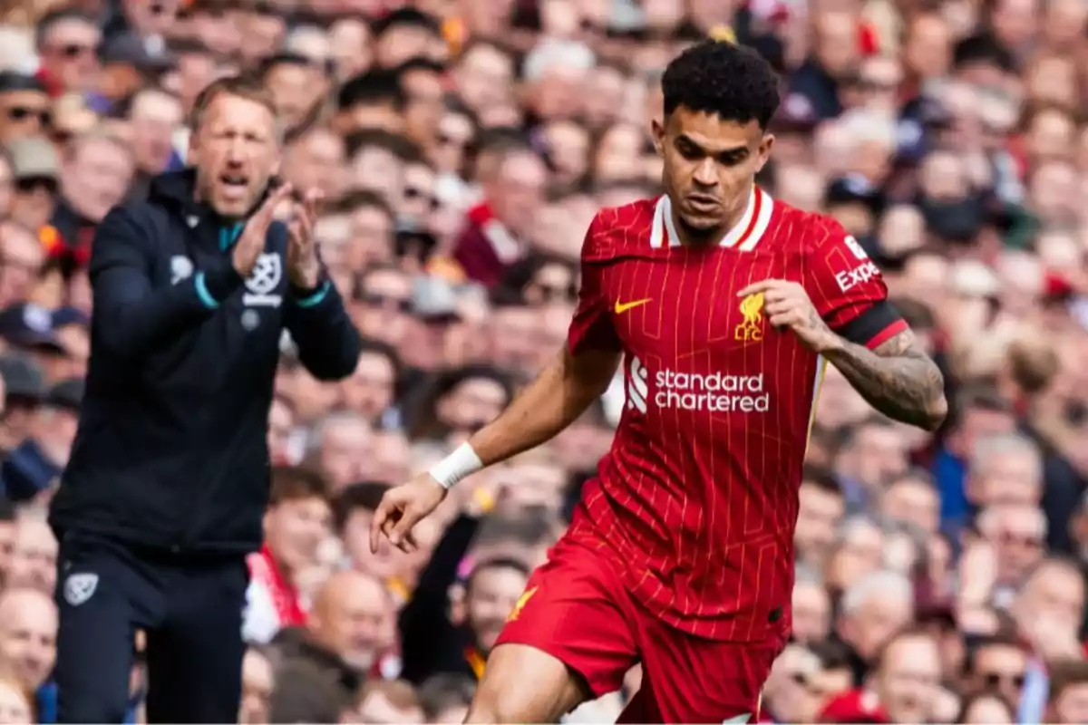 Liverpool footballer running with the ball during a match while a coach applauds in the background and the crowd watches from the stands. Liverpool footballer running with the ball during a match while a coach applauds in the background and the crowd watches from the stands.