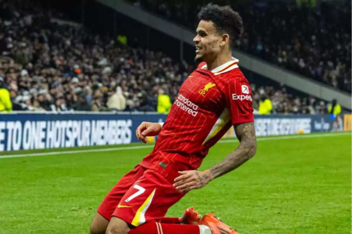 Liverpool footballer celebrating a goal on his knees on the field in front of a crowd of fans