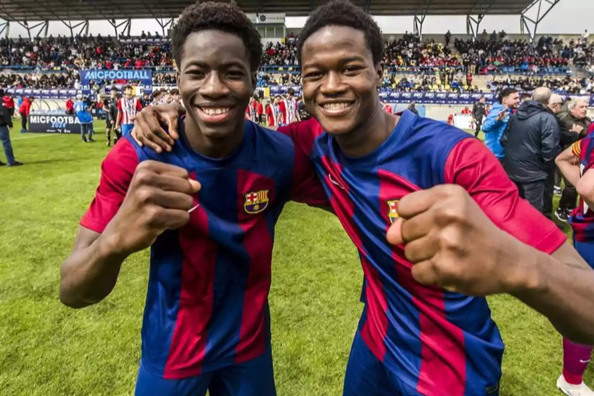 Dos jóvenes futbolistas sonríen y celebran en el campo vistiendo uniformes del FC Barcelona con una multitud en las gradas al fondo