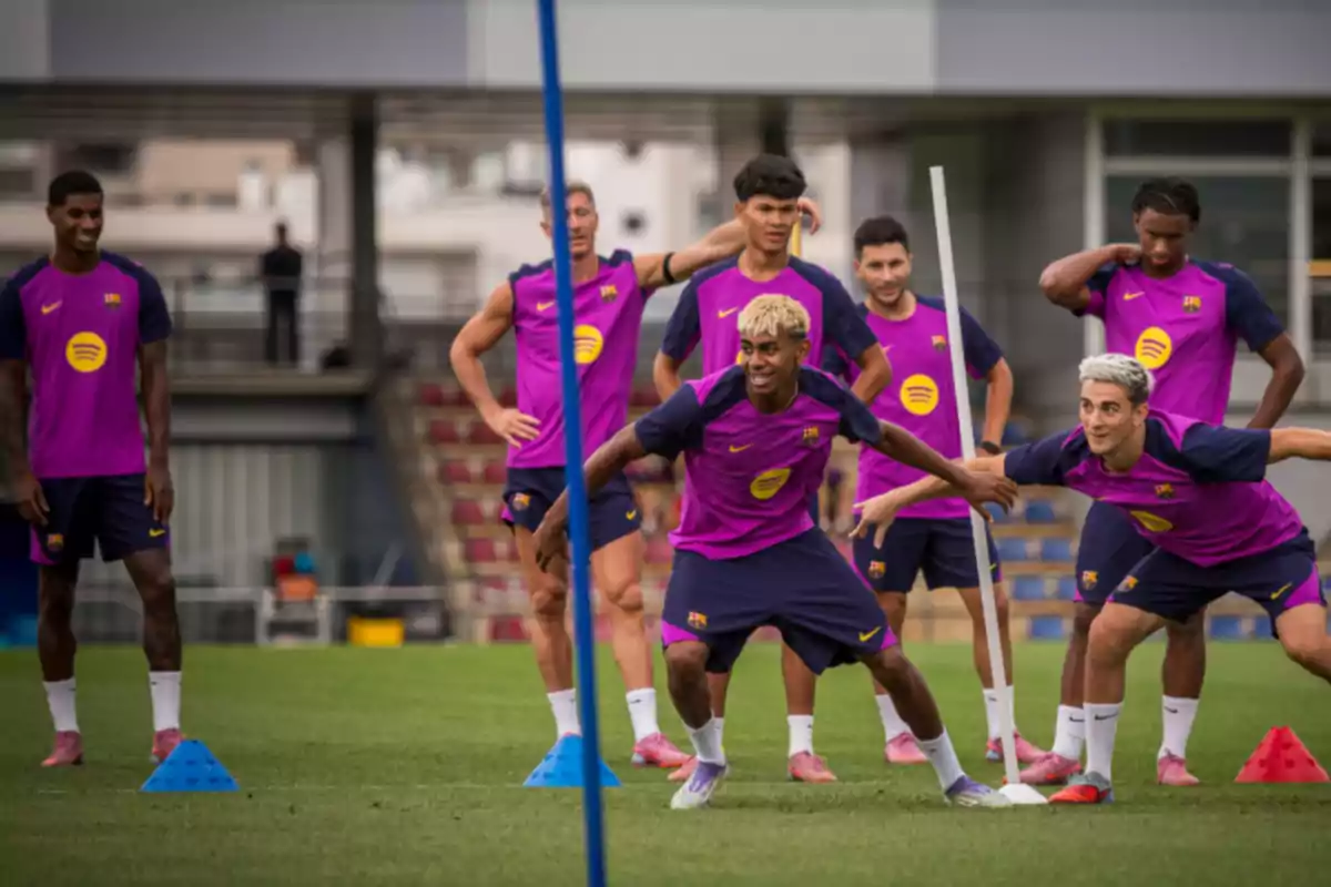 Jugadores del Barcelona entrenando en el campo con uniformes morados y conos azules y rojos sobre el césped Jugadores del Barcelona entrenando en el campo con uniformes morados y conos azules y rojos sobre el césped