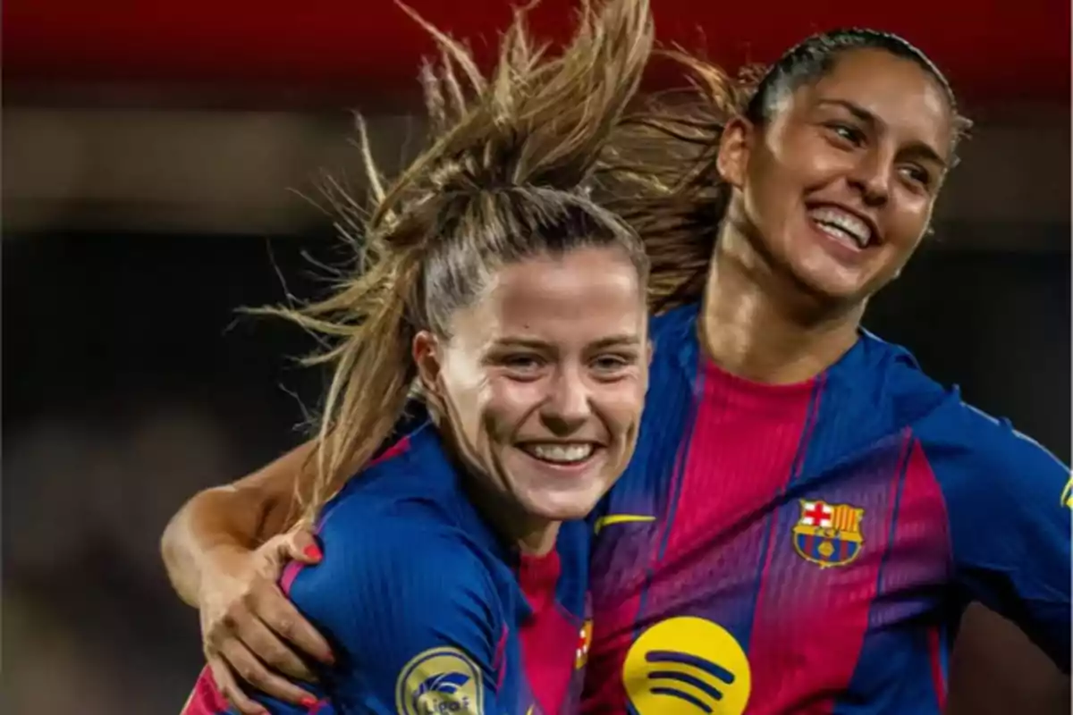 Dos jugadoras del FC Barcelona femenino celebran sonrientes durante un partido, vistiendo el uniforme azulgrana