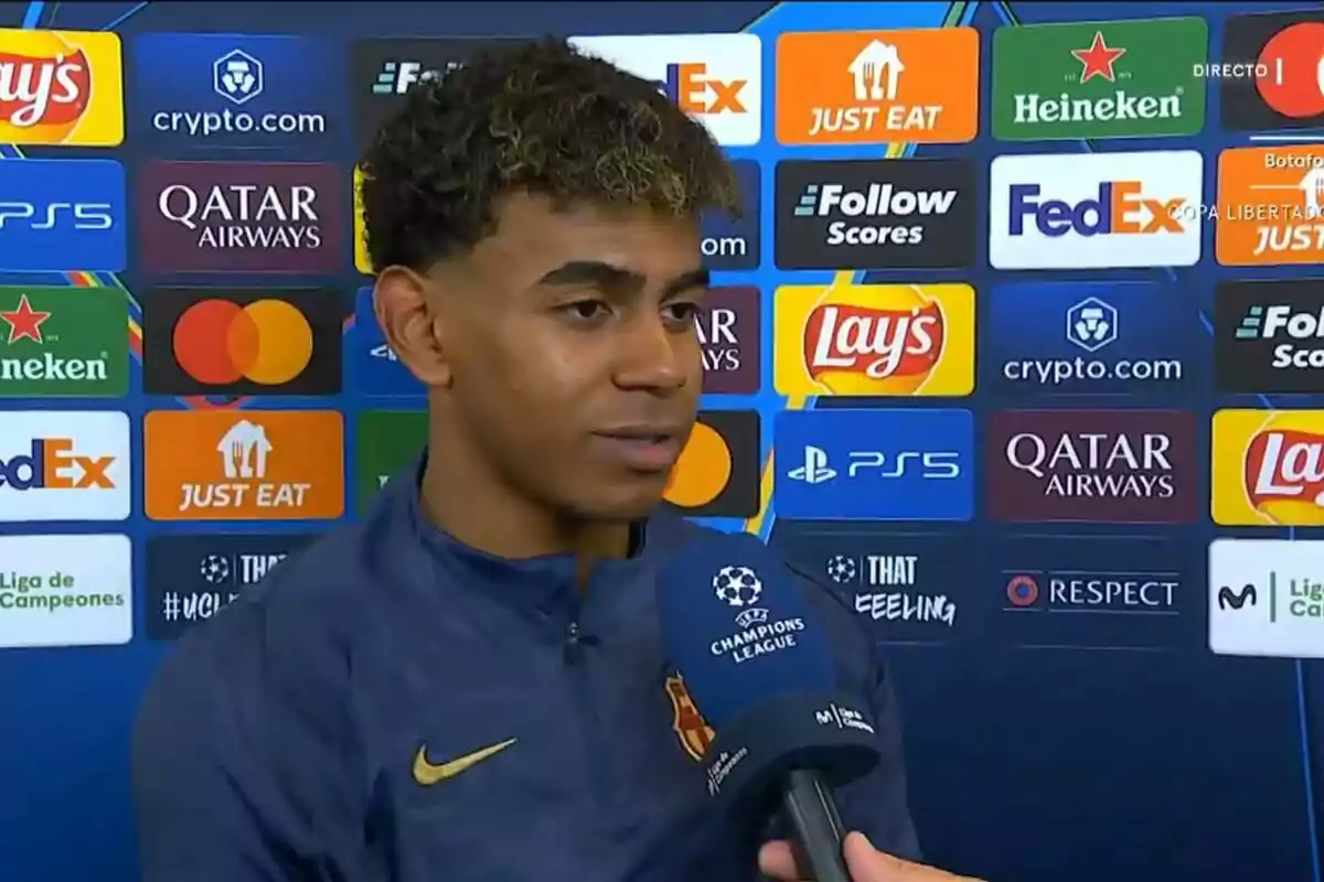 Un futbolista joven con chaqueta azul del Barcelona da una entrevista frente a un fondo con logotipos de patrocinadores de la Champions League