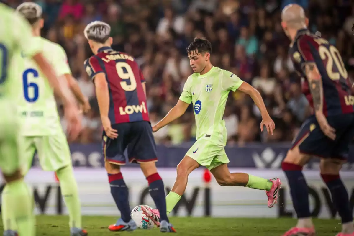 Futbolista con uniforme verde claro controla el balón mientras es rodeado por jugadores rivales con uniforme azul y rojo en un partido de fútbol profesional Futbolista con uniforme verde claro controla el balón mientras es rodeado por jugadores rivales con uniforme azul y rojo en un partido de fútbol profesional