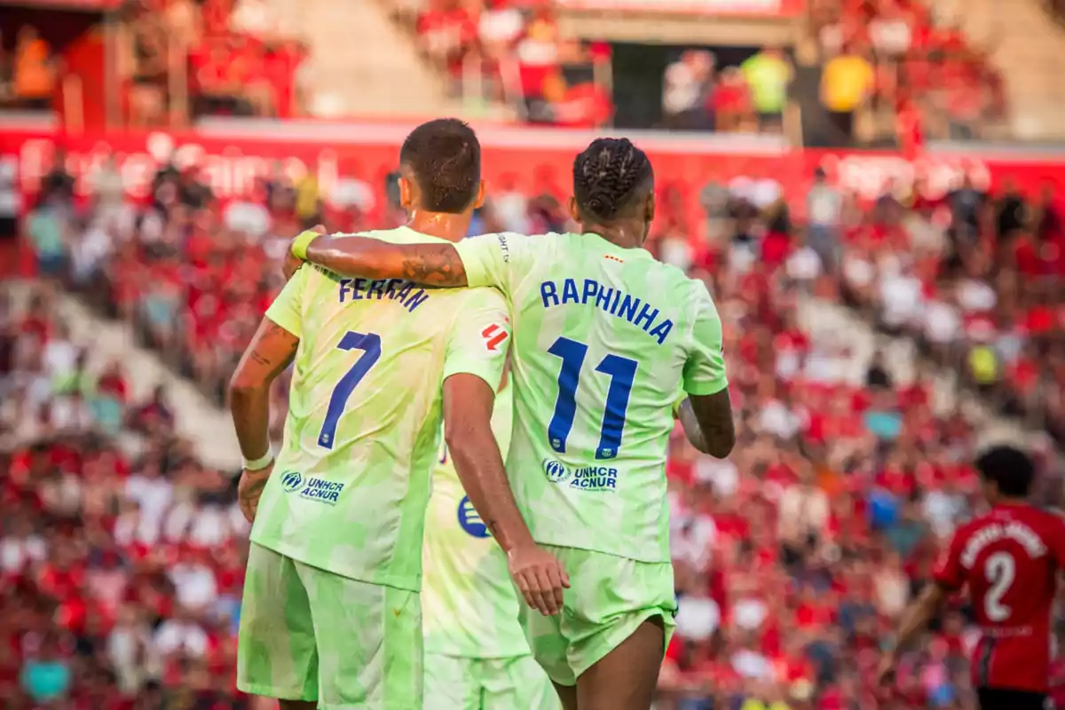 Two players in green uniforms hug each other in celebration in a stadium full of fans. Two players in green uniforms hug each other in celebration in a stadium full of fans.