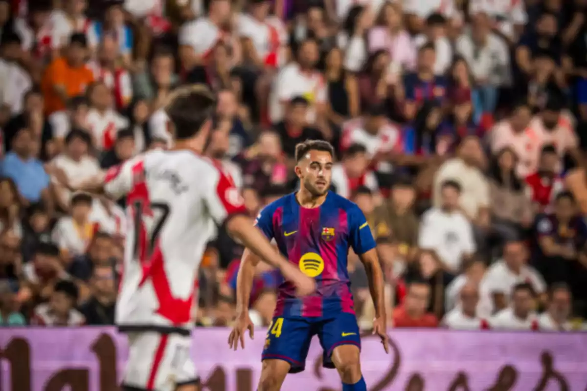 Un jugador del Barcelona observa la jugada mientras un rival del Rayo Vallecano se mueve en primer plano con el estadio lleno de aficionados al fondo Un jugador del Barcelona observa la jugada mientras un rival del Rayo Vallecano se mueve en primer plano con el estadio lleno de aficionados al fondo