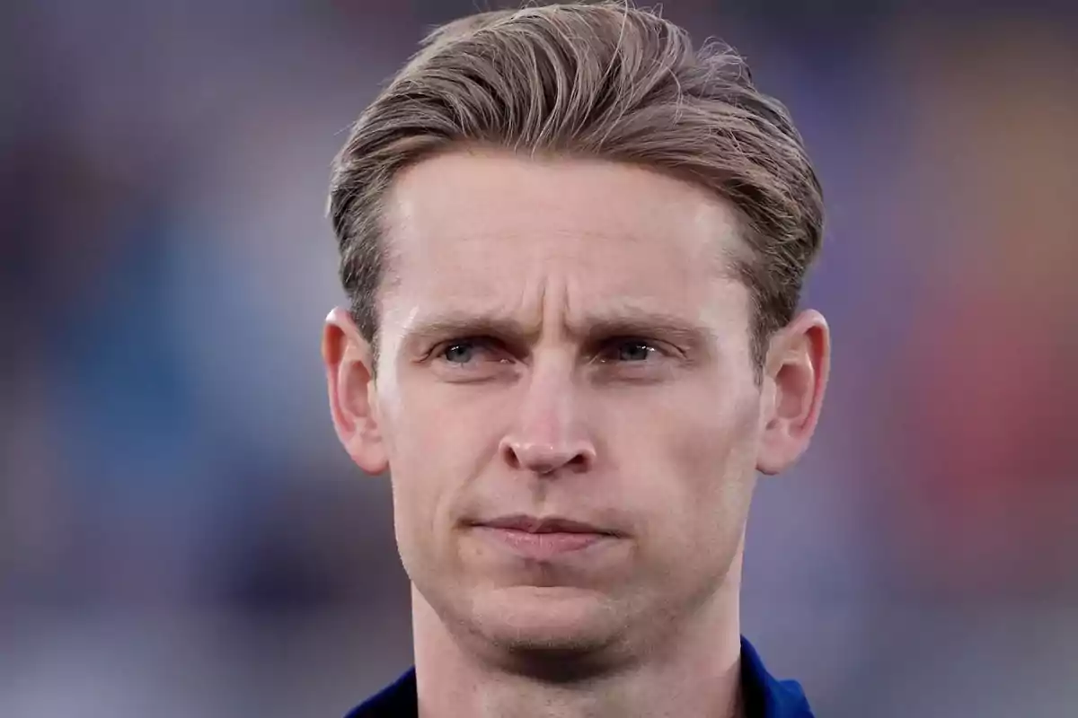 Hombre de cabello rubio corto mirando al frente con expresión seria y fondo desenfocado Hombre de cabello rubio corto mirando al frente con expresión seria y fondo desenfocado