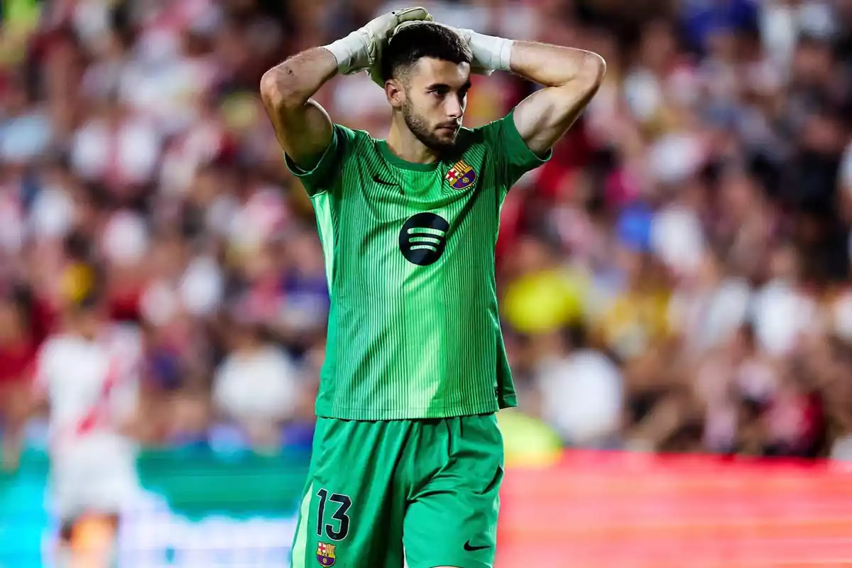 Barcelona’s goalkeeper in a green uniform and white gloves looks thoughtful with his hands on his head in a stadium full of spectators.