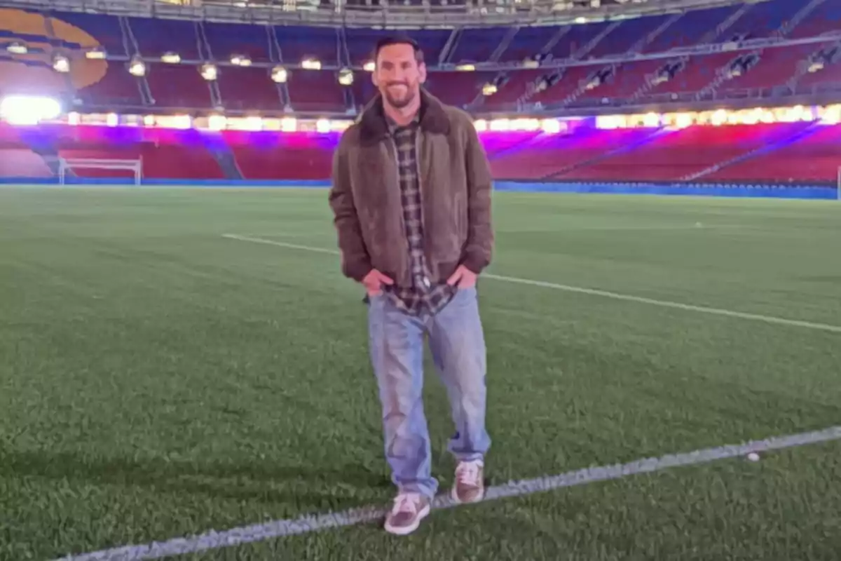 Hombre sonriente de pie sobre el césped de un estadio de fútbol vacío con gradas iluminadas al fondo Hombre sonriente de pie sobre el césped de un estadio de fútbol vacío con gradas iluminadas al fondo