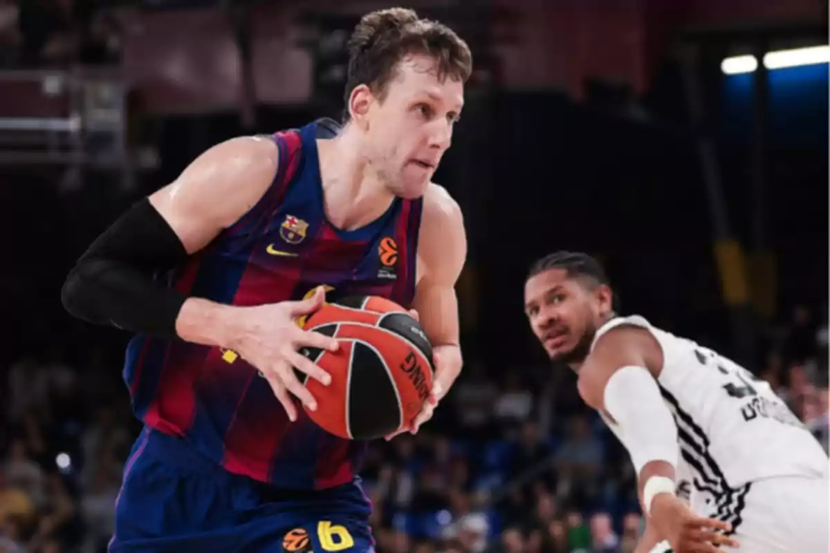 Jugador de baloncesto con uniforme azul y rojo avanza con el balón mientras un oponente con uniforme blanco lo defiende en la cancha Jugador de baloncesto con uniforme azul y rojo avanza con el balón mientras un oponente con uniforme blanco lo defiende en la cancha