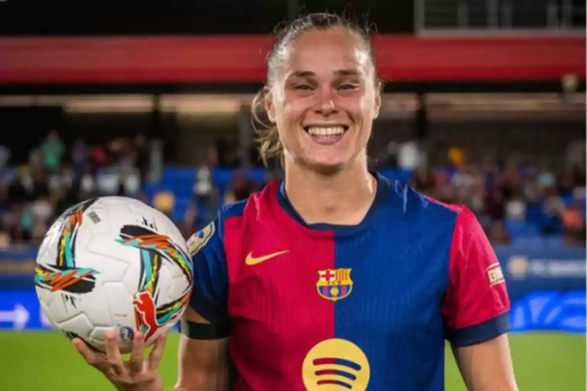 Una jugadora de fútbol sonriente con el uniforme del FC Barcelona sostiene un balón en la mano.