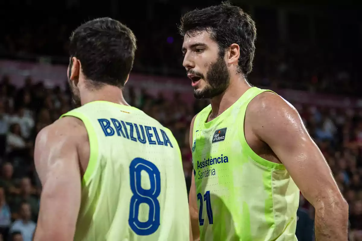 Dos jugadores de baloncesto con camisetas verdes conversan en la cancha durante un partido.