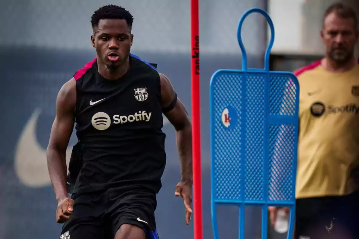 Jugador del FC Barcelona entrenando con uniforme negro y entrenador observando en el fondo. Jugador del FC Barcelona entrenando con uniforme negro y entrenador observando en el fondo.