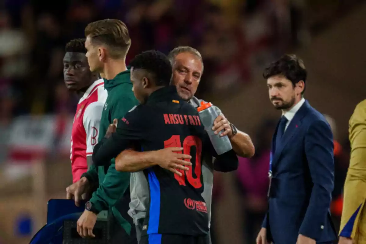 A soccer player with the number 10 on his jersey receives a hug from a man as two other men look on. A soccer player with the number 10 on his jersey receives a hug from a man as two other men look on.