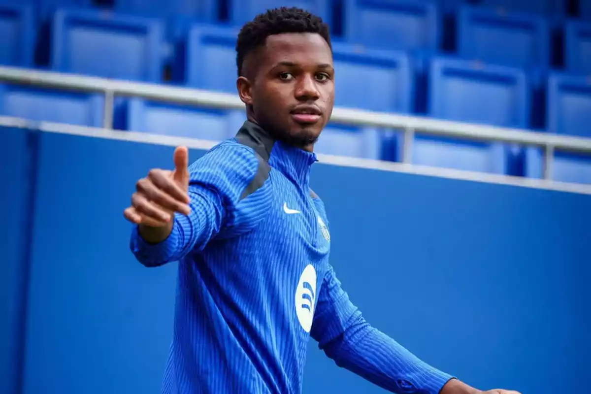 A soccer player in a blue uniform gestures with his hand in a stadium.