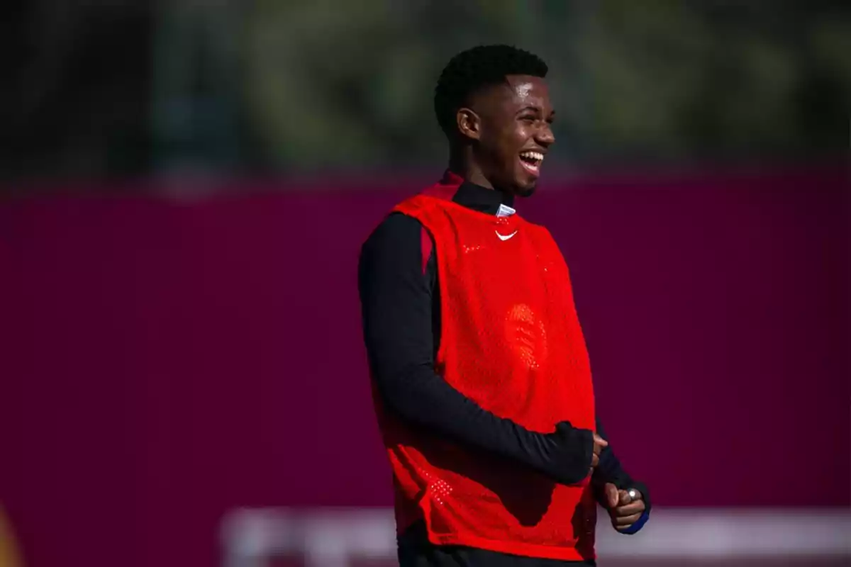 A soccer player smiles while wearing a red bib during training.