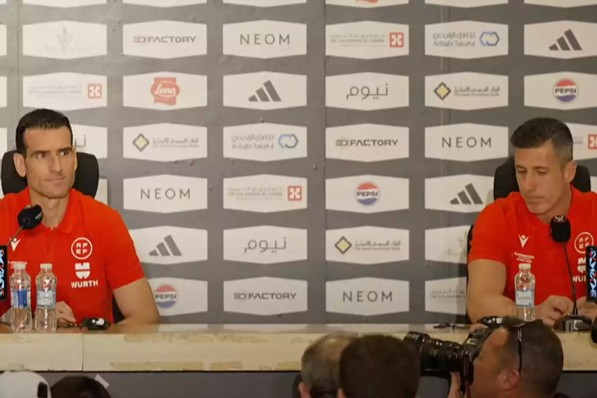 Dos personas vestidas con una camiseta roja de la Federación de fútbol española en una rueda de prensa
