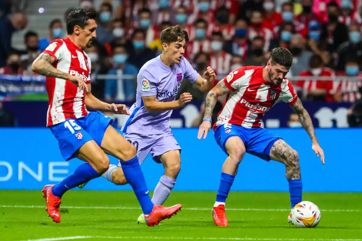 Gavi con la camiseta morada del Barça intenta robarle el balón a Rodrigo De Paul con la camiseta rojiblanca del Atlético de Madrid y el balón en su pie izquierdo