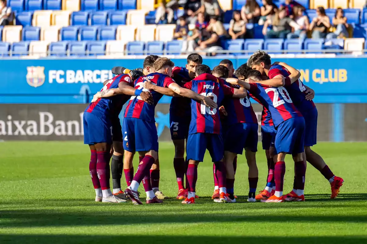 Jugadores de fútbol del Barça Atletic en un círculo abrazados en el campo antes de un partido.