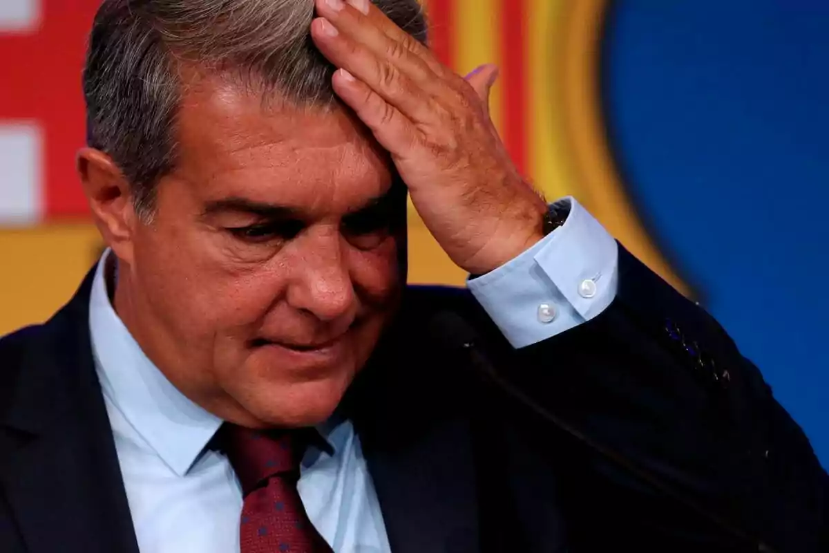 A man in a suit and tie touches his head with a thoughtful expression in front of a colorful background.