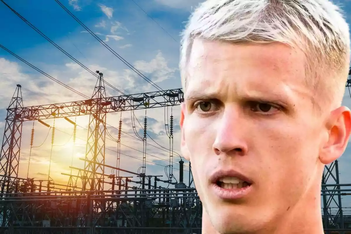 A blond-haired man appears in the foreground with a serious expression while in the background an electrical line structure is seen at sunset.