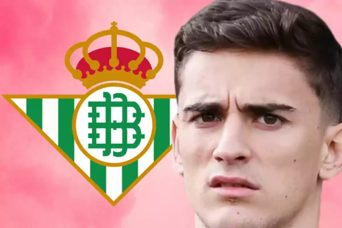 Un hombre con expresión seria frente al escudo del Real Betis sobre un fondo rosa.