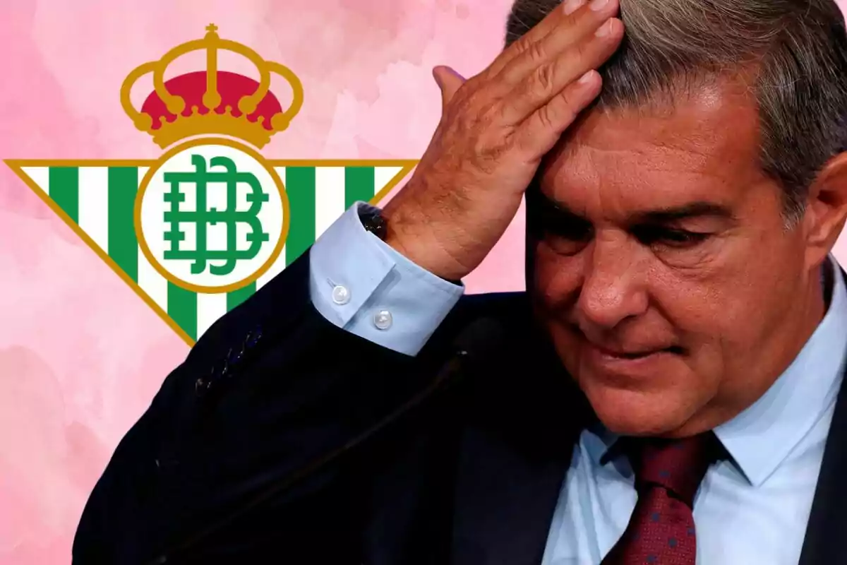 Un hombre con traje y corbata se toca la frente con la mano, con el escudo del Real Betis de fondo.