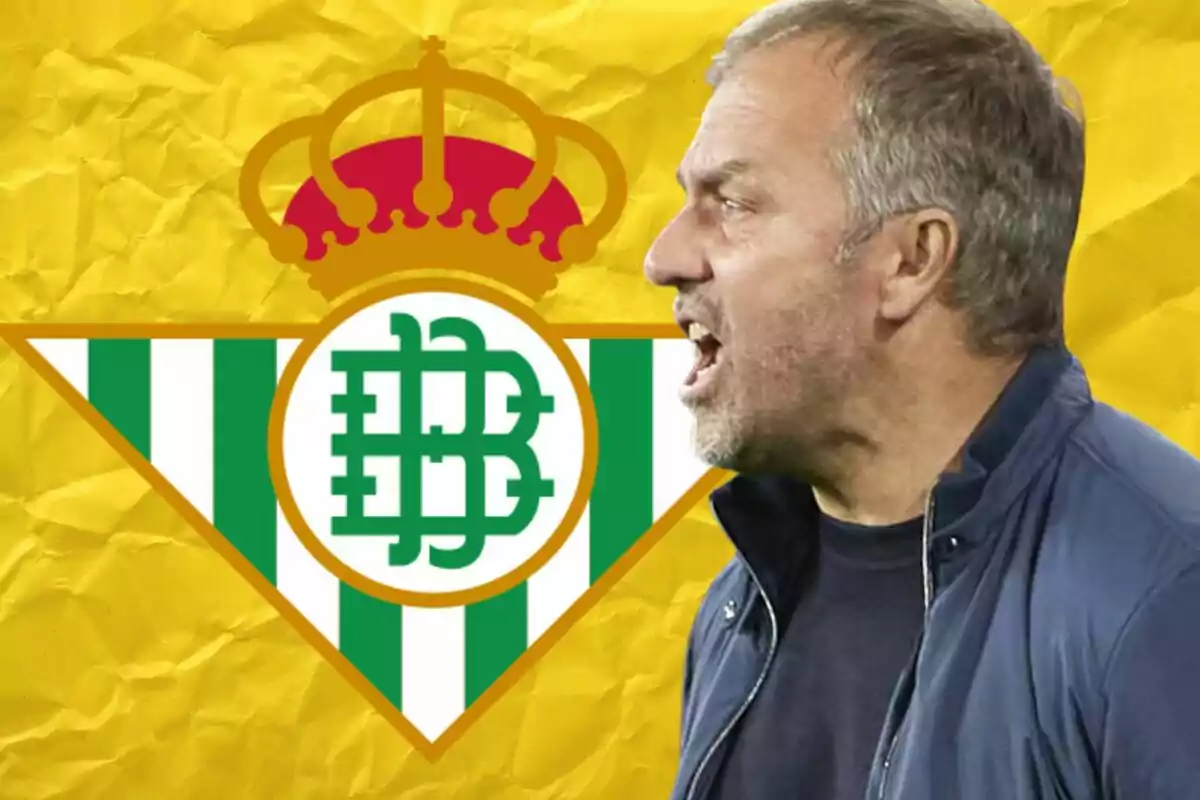 Un hombre de perfil con una chaqueta oscura frente al escudo del Real Betis sobre un fondo amarillo.