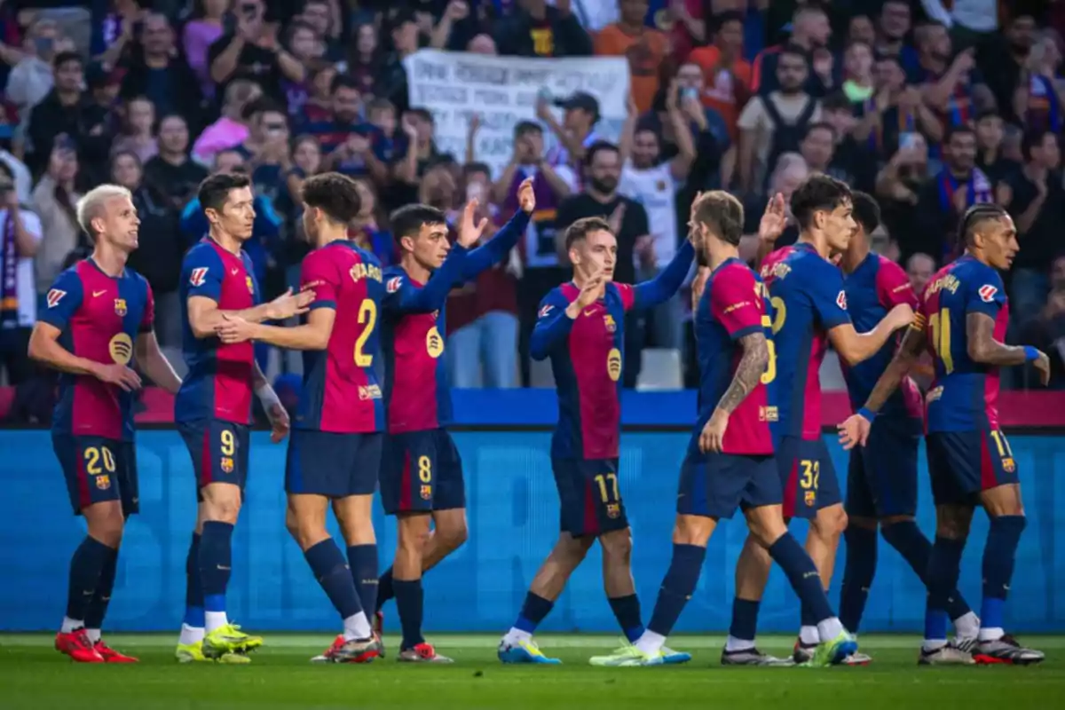 Jugadores de fútbol celebrando en el campo con aficionados de fondo.