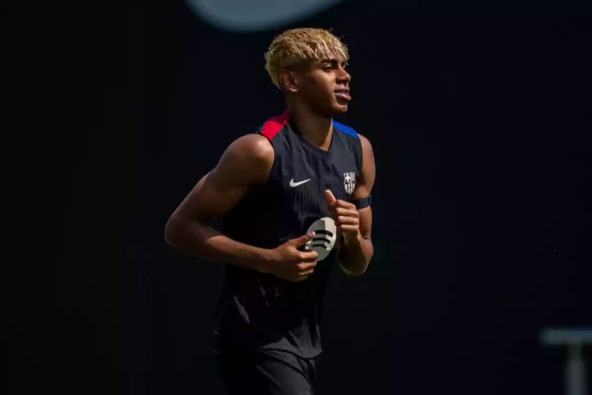 Un jugador de fútbol con cabello rubio corre durante un entrenamiento, vistiendo un uniforme oscuro con detalles en rojo y azul. Un jugador de fútbol con cabello rubio corre durante un entrenamiento, vistiendo un uniforme oscuro con detalles en rojo y azul.