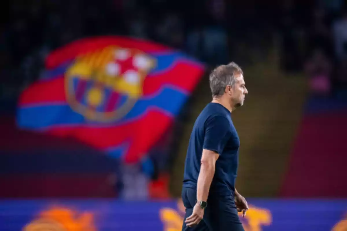 Un hombre caminando en un estadio con una bandera del FC Barcelona de fondo.