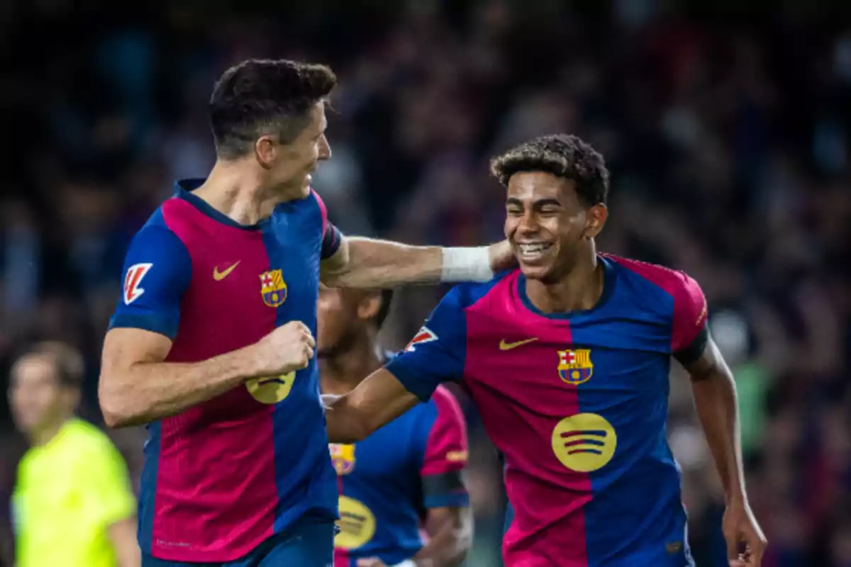 Dos jugadores de fútbol del FC Barcelona celebran en el campo con sonrisas y abrazos.