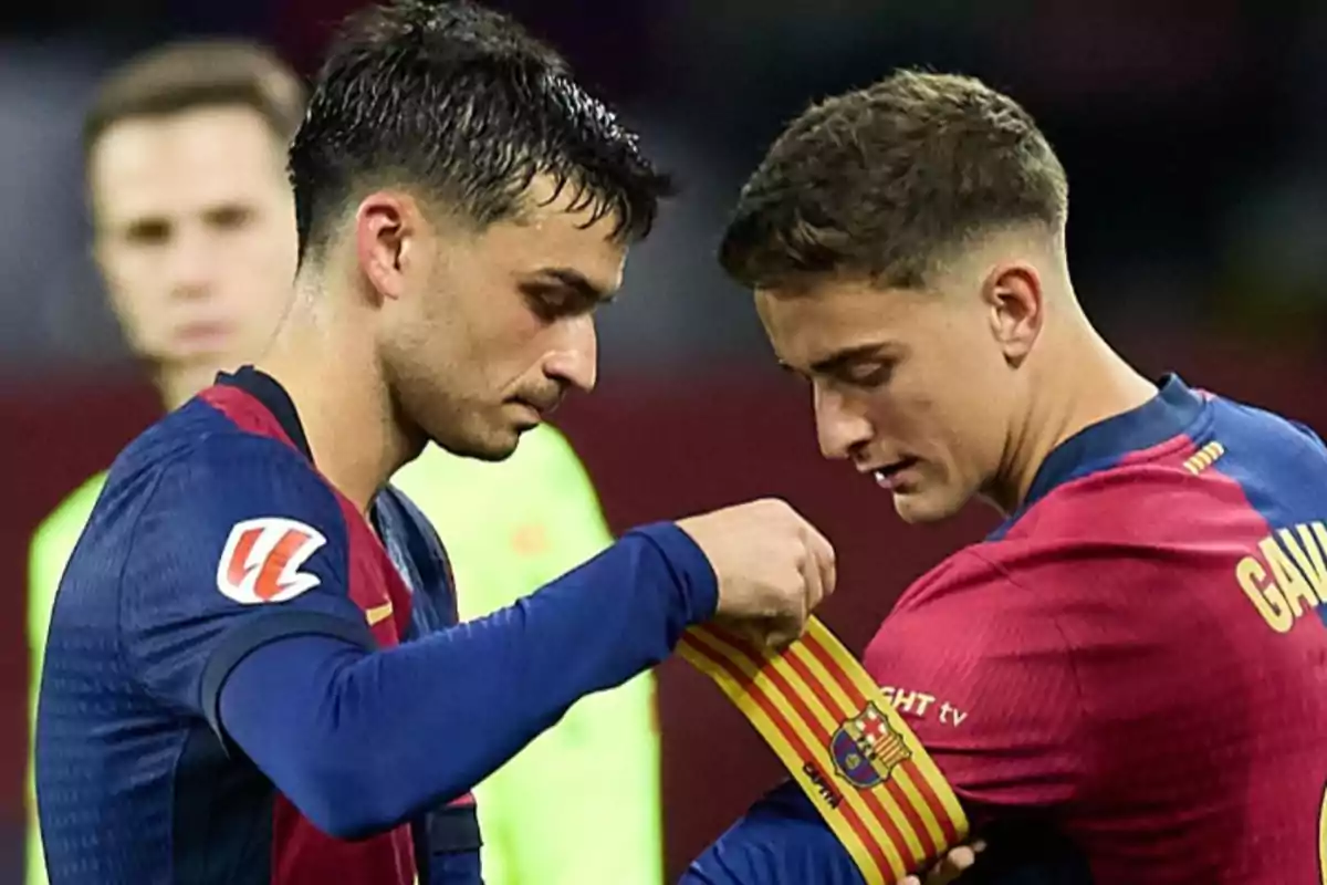 Dos jugadores de fútbol intercambian un brazalete de capitán en el campo.