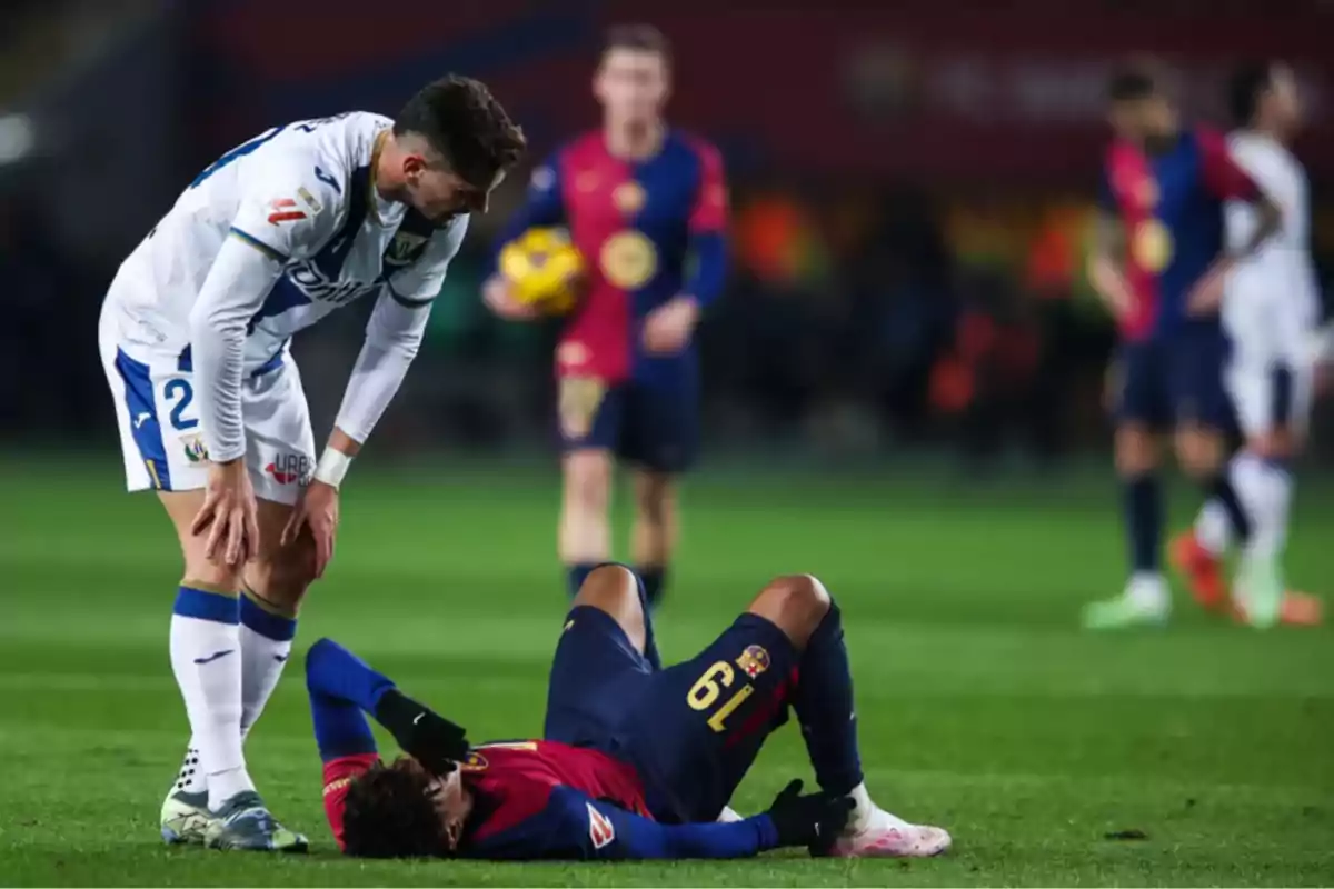 Un jugador de fútbol de pie observa a otro jugador que está tendido en el suelo durante un partido.