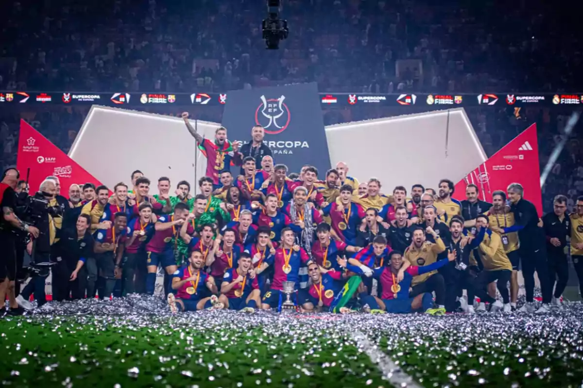 Un equipo de fútbol celebra en el campo con medallas y un trofeo, rodeados de confeti plateado.