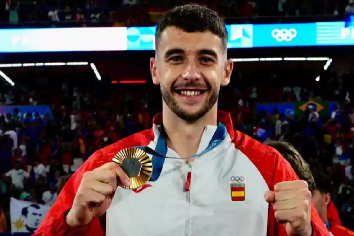 Deportista español sonriente sostiene una medalla de oro en un estadio lleno de público