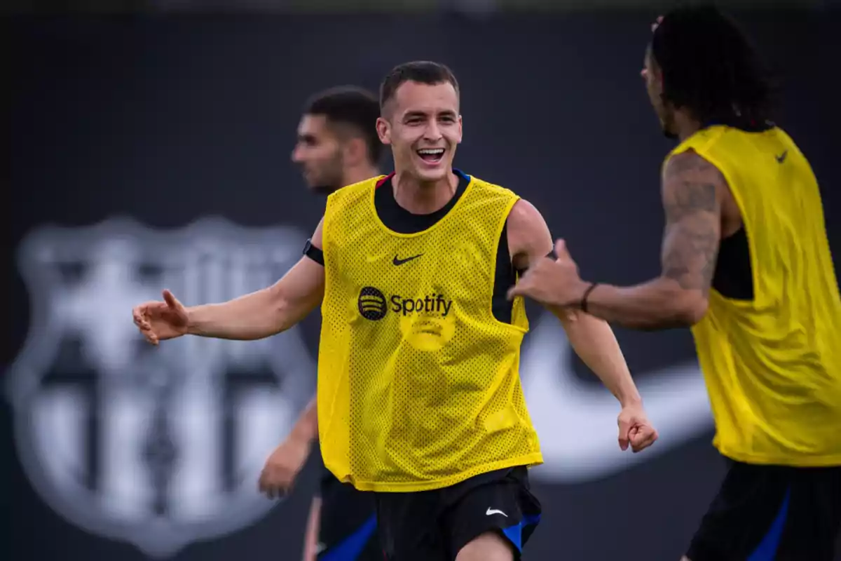 Jugadores de fútbol entrenando con petos amarillos y sonriendo en un campo con el logo de un equipo de fondo. Jugadores de fútbol entrenando con petos amarillos y sonriendo en un campo con el logo de un equipo de fondo.