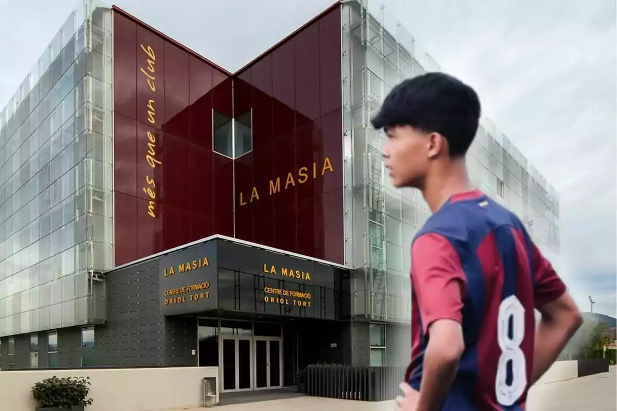 Un joven futbolista con el uniforme del FC Barcelona está de pie frente al edificio de La Masia, el centro de formación de jóvenes talentos del club.