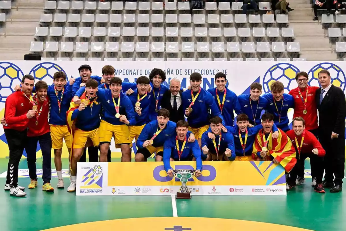 La Selección Catalana Juvenil posando con el trofeo de campeones del CESA con unas sudaderas azules y pantalones amarillos. Los entrenadores llevan sudadera roja y pantalones negros