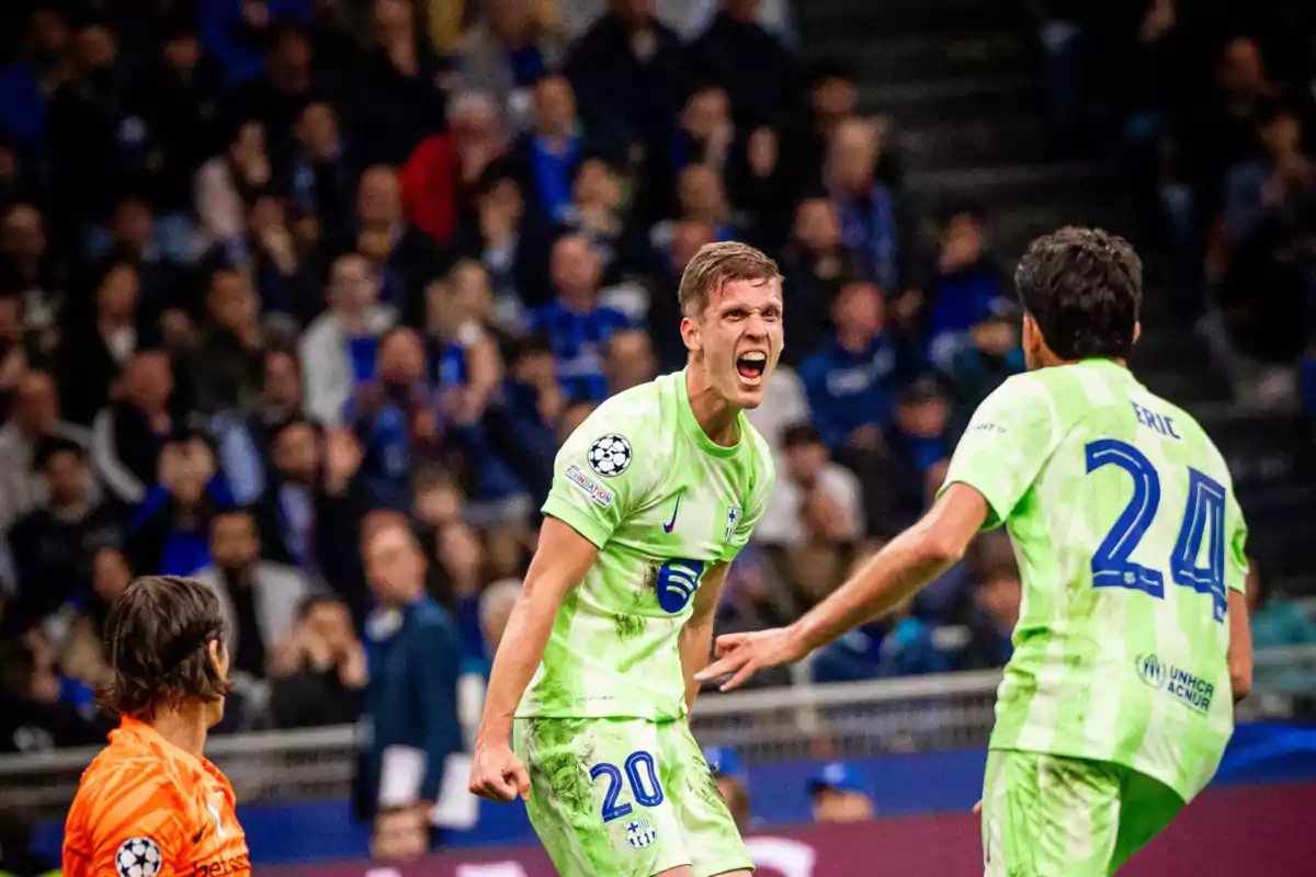 Soccer players celebrating a goal in a match, one of them with an expression of excitement and the other approaching to join the celebration, while the crowd watches from the stands. Soccer players celebrating a goal in a match, one of them with an expression of excitement and the other approaching to join the celebration, while the crowd watches from the stands.
