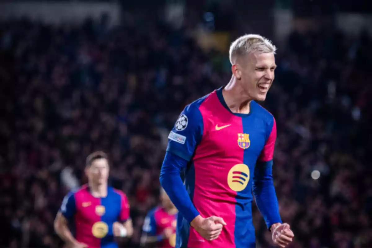 Un jugador de fútbol del FC Barcelona celebra con entusiasmo en el campo, vistiendo el uniforme azul y granate del equipo, con el logo de la Champions League visible en la manga.