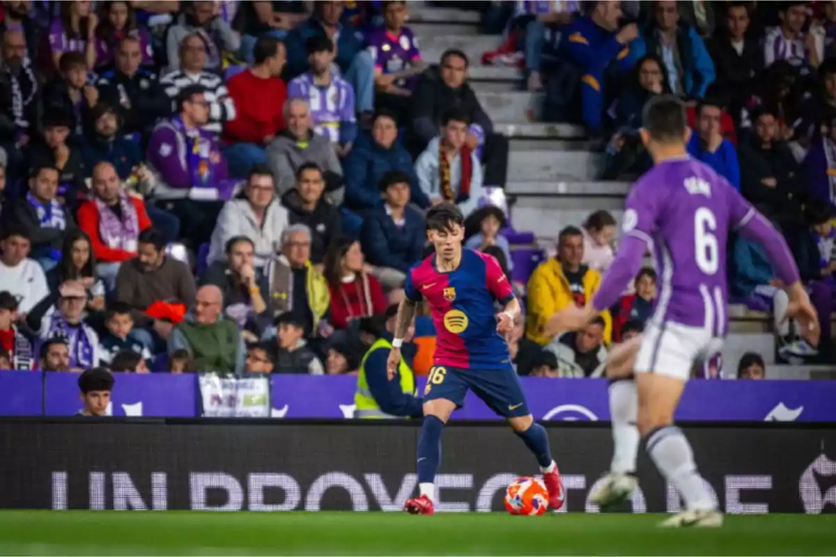 Un jugador de fútbol con el uniforme del Barcelona controla el balón en el campo mientras un oponente del equipo contrario se acerca, con una multitud de espectadores en las gradas al fondo. Un jugador de fútbol con el uniforme del Barcelona controla el balón en el campo mientras un oponente del equipo contrario se acerca, con una multitud de espectadores en las gradas al fondo.