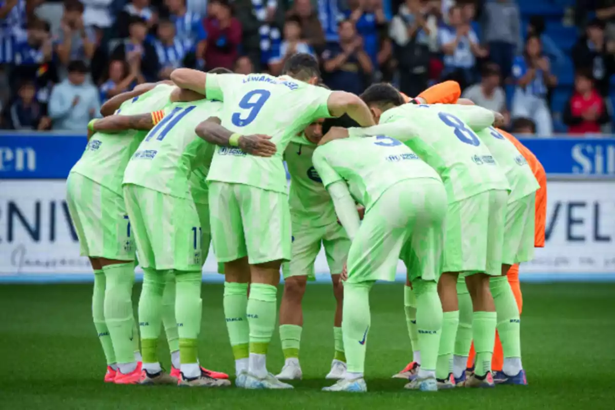 Un equipo de fútbol en uniforme verde se reúne en un círculo en el campo antes de un partido.