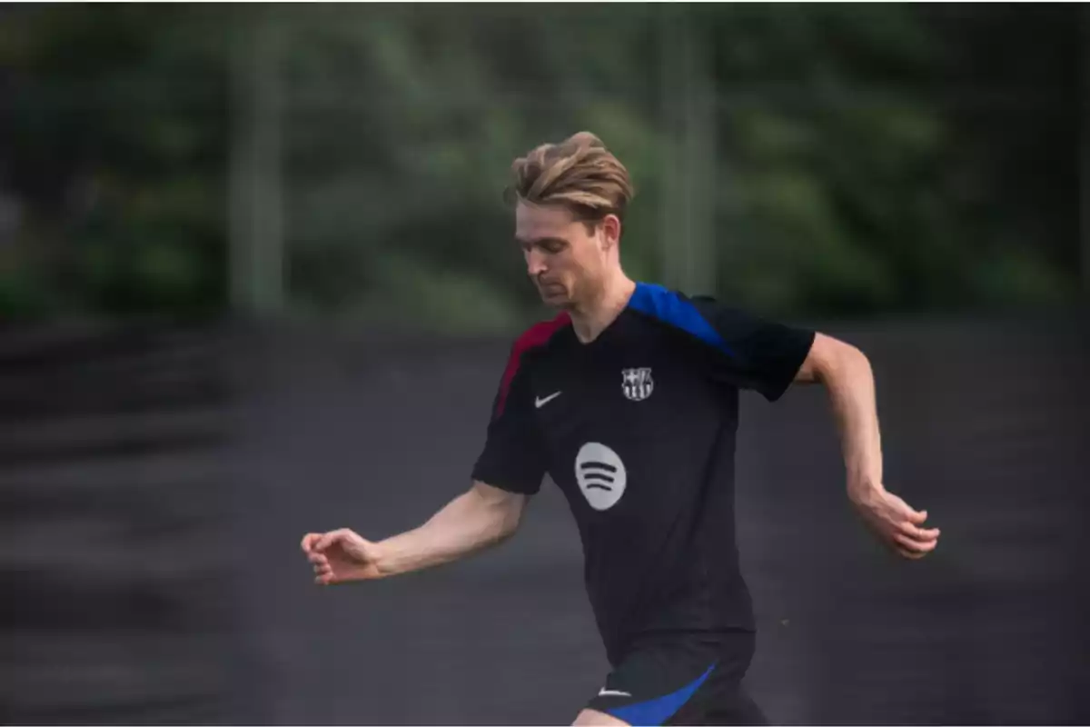 A soccer player running on the field in a black uniform with blue and red details.