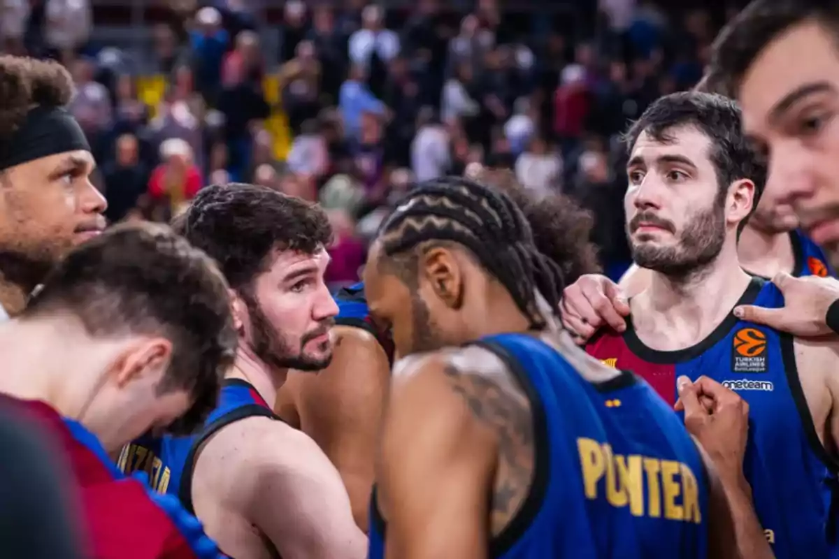 Jugadores de baloncesto en un momento de concentración durante un partido con el público de fondo.