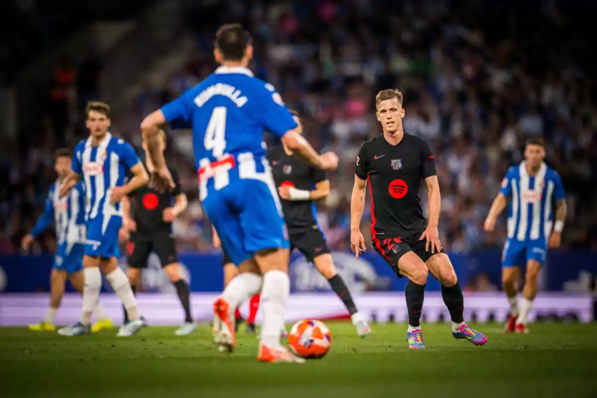 Jugadores de fútbol en acción durante un partido, uno con uniforme azul y blanco y otro con uniforme negro, con el balón en el campo. Jugadores de fútbol en acción durante un partido, uno con uniforme azul y blanco y otro con uniforme negro, con el balón en el campo.