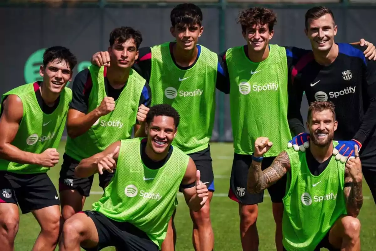 Un grupo de jugadores de fútbol sonríe y posa para una foto durante un entrenamiento, todos llevan petos verdes con el logo de Spotify.