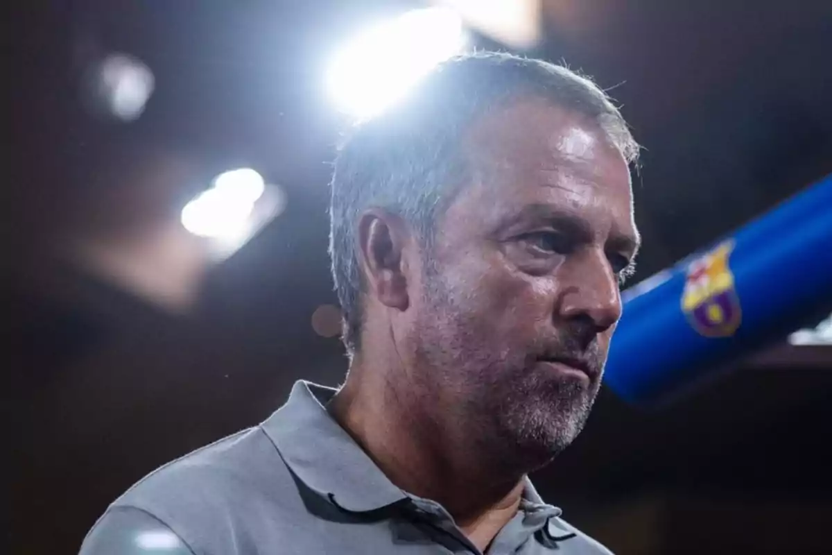 Hombre de mediana edad con barba y cabello corto, vestido con una camiseta polo gris, con una luz brillante detrás de él y un fondo oscuro.