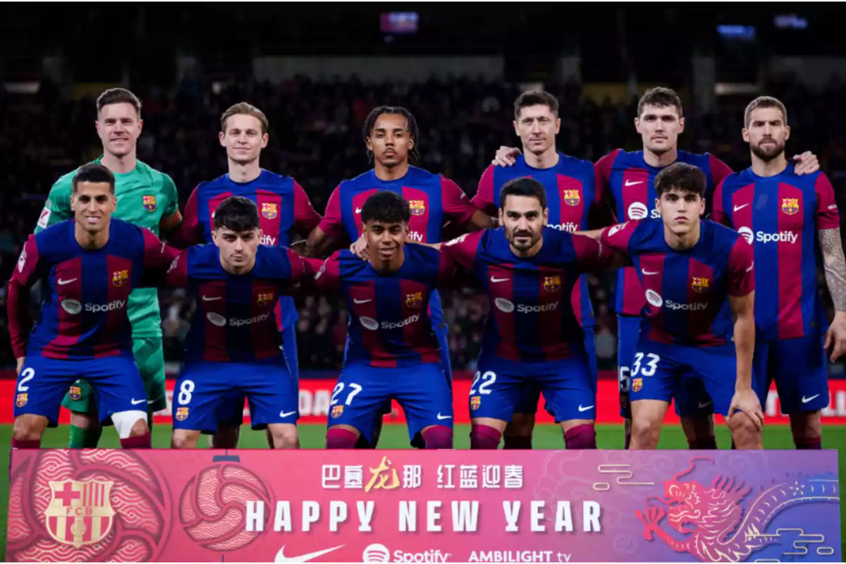 se puede ver la imagen de 11 futbolistas vestidos de azul y rojo, entan algunos de pie y otros agachados, encima de un césped y de fondo una grada con gente en lo que parece un estadio de futbol